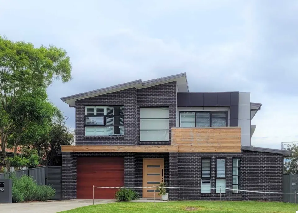 Dark brick two-storey home with timber cladding and a red garage door